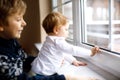 Happy adorable kid boy and cute baby girl sitting near window and looking outside on snow on Christmas day or morning Royalty Free Stock Photo