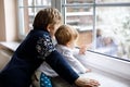 Happy adorable kid boy and cute baby girl sitting near window and looking outside on snow on Christmas day or morning Royalty Free Stock Photo