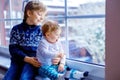 Happy adorable kid boy and cute baby girl sitting near window and looking outside on snow on Christmas day or morning Royalty Free Stock Photo