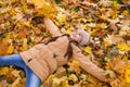 Happy adorable little girl lying on the fallen leaves arms outstretched and holding the bouquets of yellow maple leaves in her han Royalty Free Stock Photo