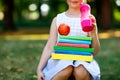 Happy adorable little kid girl reading book and holding different colorful books, apples and water bottle on first day