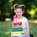 Happy adorable little kid girl reading book and holding different colorful books, apples and water bottle on first day