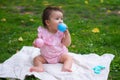 happy and adorable 7 or 8 months old baby girl playing with ball toy cheerful sitting on towel lying on grass city park in Royalty Free Stock Photo