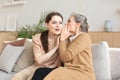 Happy adult daughter whispering secret to her middle mother at home, gossiping, sharing secret