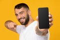 Happy adult european man in white t-shirt pointing finger at phone with blank screen