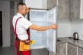 Happy adult handyman repairing refrigerator in domestic kitchen Royalty Free Stock Photo