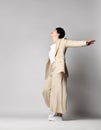 Happy adult woman in beige business casual pantsuit and sneakers stands sideways, dancing. Stylish business female wear