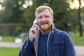 Happy adult red haired man blue eyes, beard, mustache smiling, talking smartphone, mobile. stylish young ginger bearded guy using Royalty Free Stock Photo