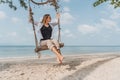 Happy adult young woman in sunglasses and white blouse swinging on a swing on a tropical beach Royalty Free Stock Photo