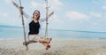 Happy adult young woman in sunglasses and white blouse swinging on a swing on a tropical beach Royalty Free Stock Photo