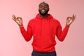 Happy african american bearded man in red hoodie meditating found peace nirvana smiling delighted close eyes relaxed