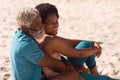 Happy african american bearded senior man embracing mature woman sitting on sandy beach in summer Royalty Free Stock Photo