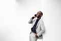Happy african american businessman talking with cellphone while leaning against white wall Royalty Free Stock Photo