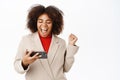 Happy african american businesswoman looking at mobile phone and celebrates, laughs, triumphing, winning on smartphone Royalty Free Stock Photo