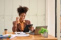 Happy African American businesswoman received good news, celebrating success with arms up in front of laptop at office Royalty Free Stock Photo