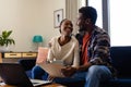 Happy african american couple embracing and doing paperwork using laptop at home Royalty Free Stock Photo