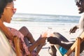 Happy african american couple sitting in deckchairs making a toast with bottles on sunny beach Royalty Free Stock Photo