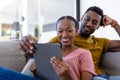 Happy african american couple smiling and embracing and using tablet on couch at home Royalty Free Stock Photo