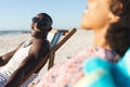 Happy african american couple in sunglasses sitting in deckchairs laughing on sunny beach Royalty Free Stock Photo