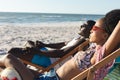 Happy african american couple in sunglasses sitting in deckchairs relaxing on sunny beach by the sea Royalty Free Stock Photo