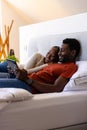 Happy african american couple using tablet lying on bed in bedroom Royalty Free Stock Photo