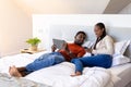 Happy african american couple using tablet and smartphone lying on bed in bedroom Royalty Free Stock Photo
