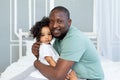 Happy African-American dad hugs baby daughter on bed at home, happy family