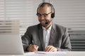 Happy African American employee in headset making notes, using laptop Royalty Free Stock Photo