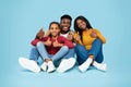 Happy african american family gesturing thumbs up and smiling, parents and their daughter sitting over blue background Royalty Free Stock Photo