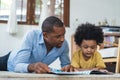 Happy African American family spending time together at home. Cute black son and his handsome father are reading a book while Royalty Free Stock Photo