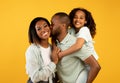 Happy african american family of three with adorable daughter, posing and smiling to camera over yellow background Royalty Free Stock Photo