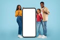 Happy african american family of three showing ok signs near huge cellphone with blank white screen, mockup Royalty Free Stock Photo