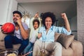 Happy African American family of three watching tv and cheering sport games on sofa