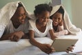 Happy African American family under blanket and using digital tablet on bed in bedroom Royalty Free Stock Photo