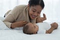 Happy African American family, young mother smiling holding her cute newborn baby girl hand and lying on bed together at bedroom Royalty Free Stock Photo