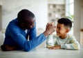 Happy african american father competing in arm-wrestling with his son, enjoying time together at home