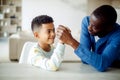 Happy african american father competing in arm-wrestling with his son, enjoying time together at home Royalty Free Stock Photo