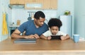 Happy African American father and his little son using digital tablet sits together at table in kitchen room. Caring dad and small Royalty Free Stock Photo