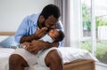 Happy African American father man sitting holding and kissing newborn son baby on a bed in the bedroom at home Royalty Free Stock Photo