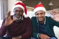 Happy african american father and son in christmas hats having video call at home waving Royalty Free Stock Photo