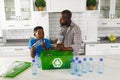 Happy african american father and son in kitchen talking and sorting plastic waste for recycling Royalty Free Stock Photo