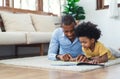 Happy African American father and son are reading a book and smiling while lying on floor spending time together at home. Children Royalty Free Stock Photo