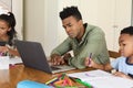 Happy african american father using laptop, daughter and son doing homework at home Royalty Free Stock Photo