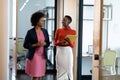 Happy african american female business colleagues walking through corridor holding documents talking Royalty Free Stock Photo
