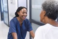 Happy african american female doctor talking with senior female patient in hospital corridor Royalty Free Stock Photo