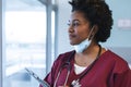 Happy african american female doctor wearing scrubs and face mask, looking through window Royalty Free Stock Photo