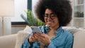 Happy African American girl holding cell mobile phone using smartphone device gadget at home smiling young woman using Royalty Free Stock Photo