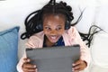 Happy african american girl lying on couch, listening to music and using tablet at home, copy space Royalty Free Stock Photo