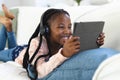 Happy african american girl lying on couch, listening to music and using tablet at home, copy space Royalty Free Stock Photo