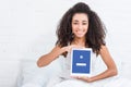 Happy african american girl showing digital tablet with facebook on screen in bed